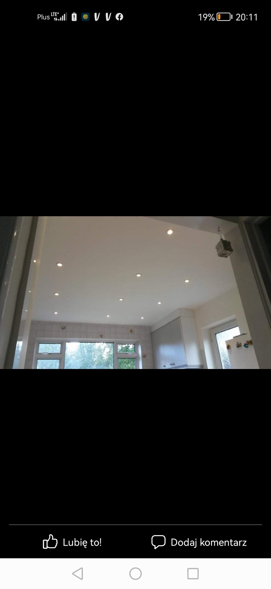 Jasna kuchnia po remoncie z białymi ścianami, nowymi płytkami nad oknem i punktowym oświetleniem sufitowym.