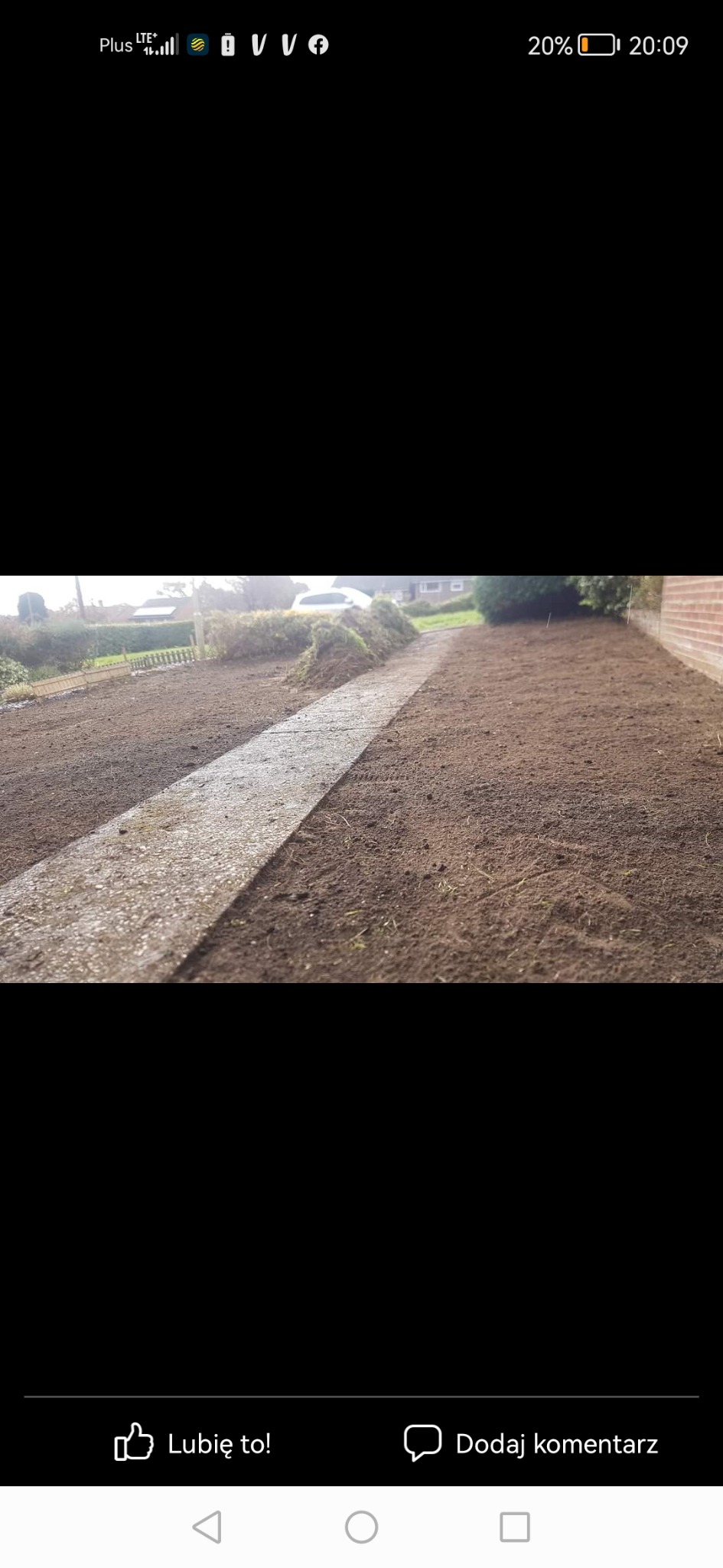 Przygotowany teren pod trawnik z widoczną ścieżką z szarej kostki, świeżo nawieziona ziemia, w tle widoczny ogród i dom.