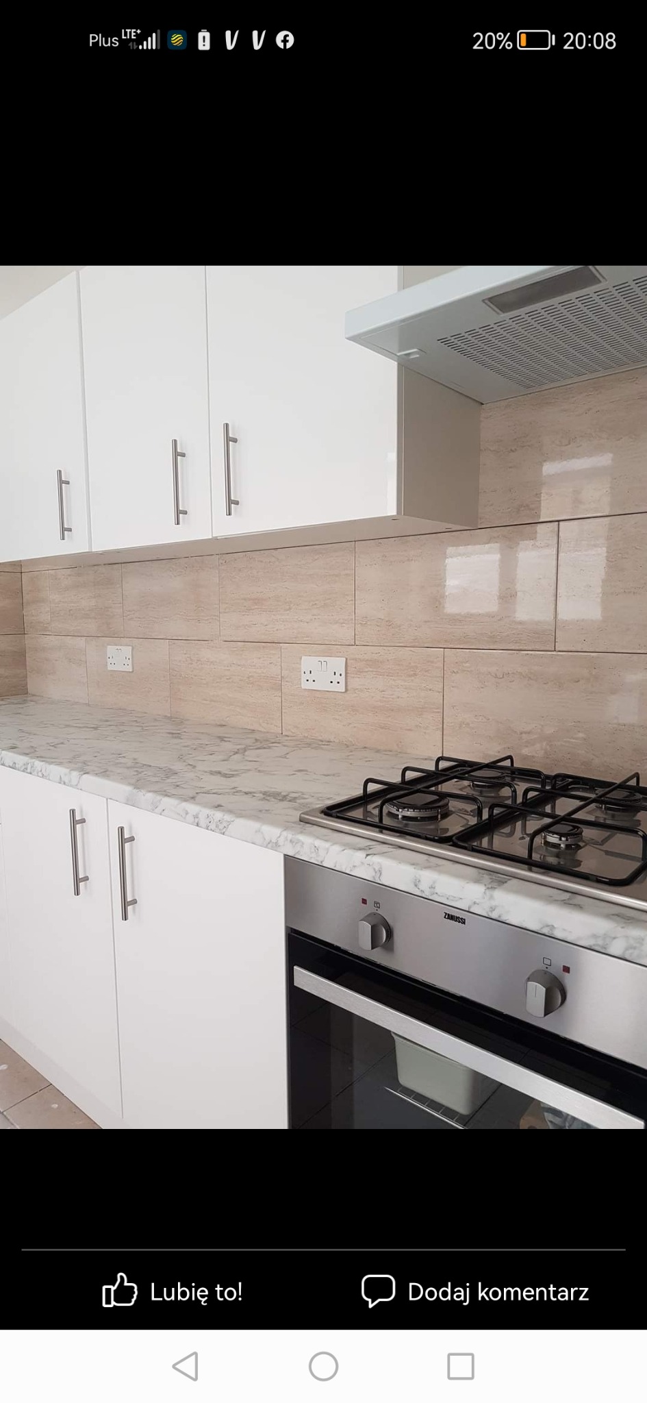 Nowoczesna kuchnia z białymi szafkami, marmurowym blatem i beżowymi płytkami imitującymi trawertyn na ścianie, z widoczną płytą gazową i piekarnikiem marki Zanussi.