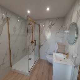 MD-BUD - Nowoczesna łazienka z kabiną prysznicową ze złotymi ramami, umywalką na szafce, toaletą z drewnianą obudową spłuczki i okrągłym lustrem na ścianie wyłożonej marmurowymi płytkami.