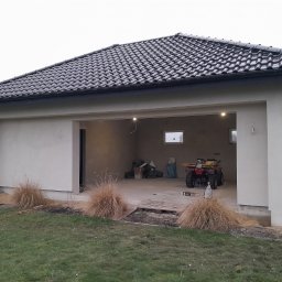 MD-BUD - Nowo otynkowany garaż z czarną dachówką, widoczne ślady po pracach budowlanych, wewnątrz quad i materiały budowlane.