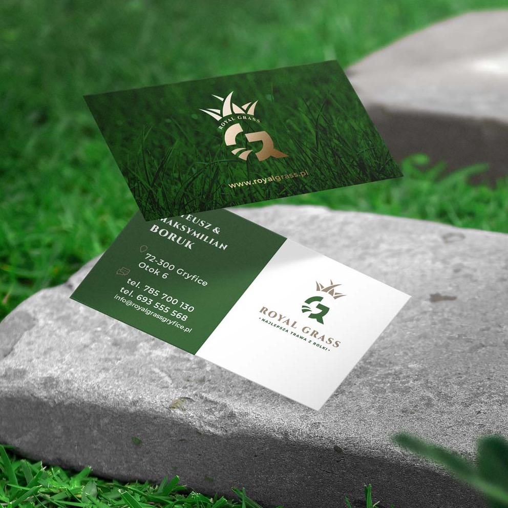 Dwie wizytówki firmy Royal Grass prezentowane na kamieniu, z logo w kolorze złotym i motywem trawy w tle, jedna z adresem i numerami telefonów, druga z adresem strony internetowej.
