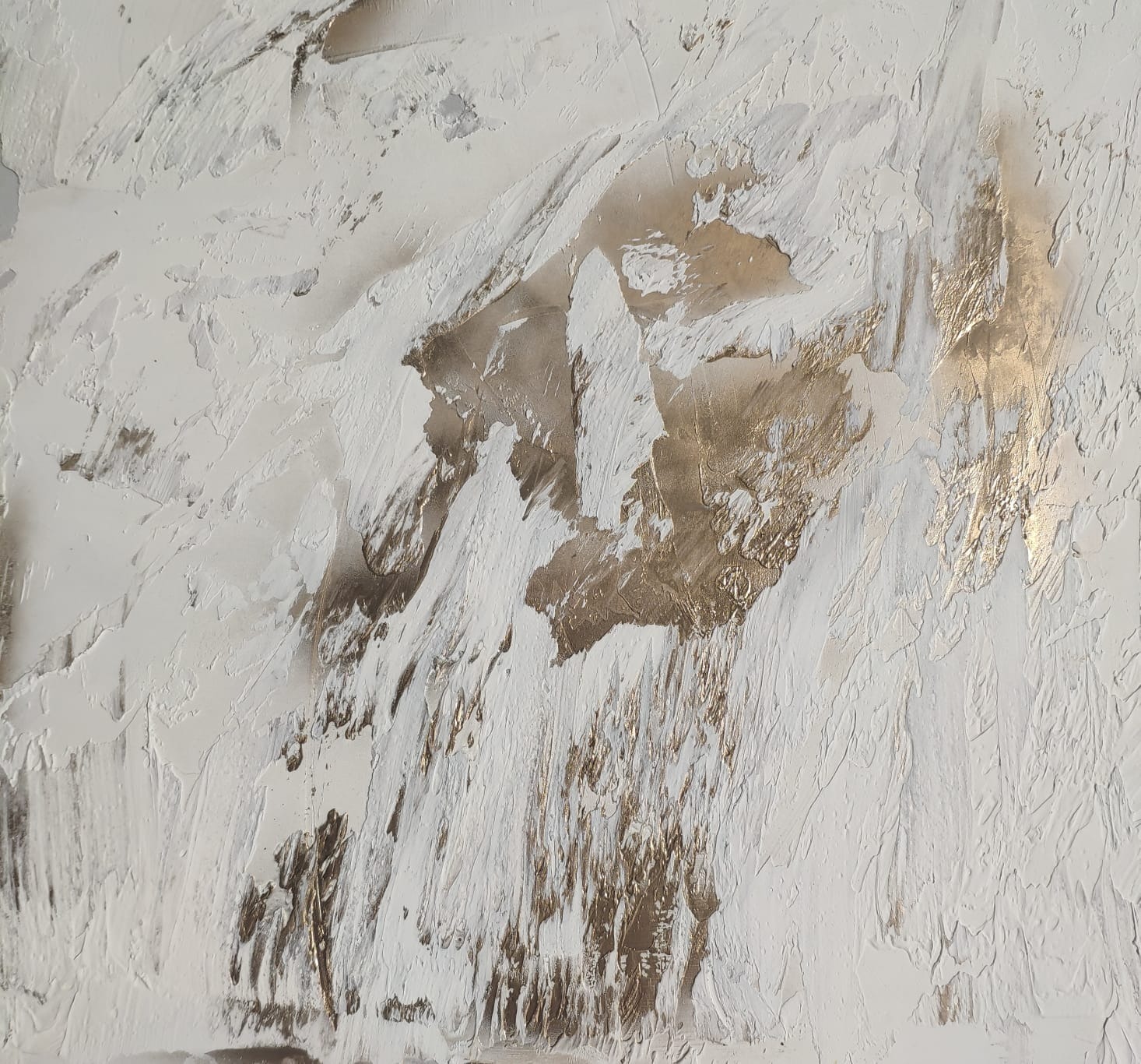 Tekstura ściany pokryta grubą warstwą białej farby z elementami złotej farby, tworząca abstrakcyjny wzór przypominający górski krajobraz.