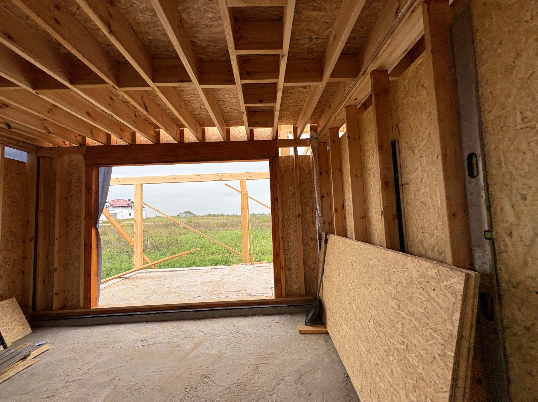 Surowy szkielet drewniany domu w budowie z widoczną konstrukcją dachu, ścianami z płyt OSB i otwartym przejściem na zewnątrz z widokiem na krajobraz.