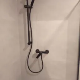 Czarny zestaw prysznicowy z deszczownicą i baterią zamontowany na jasnych, płytkach w łazience. Widok na ścianę z prysznicem.