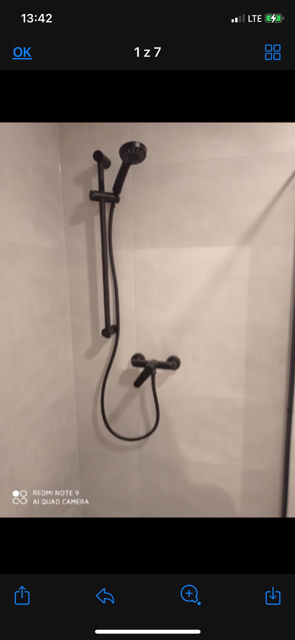 Czarny zestaw prysznicowy z deszczownicą i baterią zamontowany na jasnych, płytkach w łazience. Widok na ścianę z prysznicem.