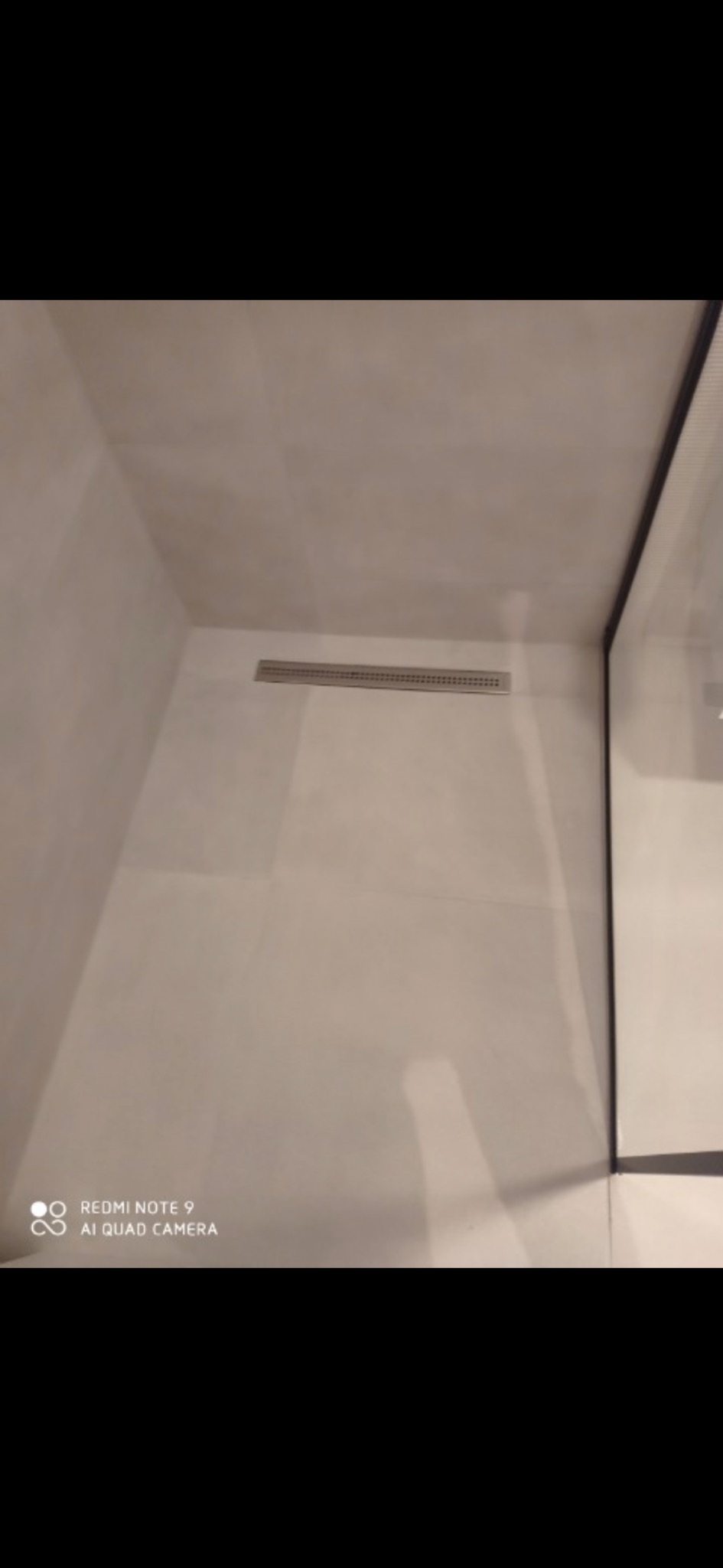 Ukończona kabina prysznicowa z odpływem liniowym w posadzce, wykończona jasnymi, kwadratowymi płytkami.