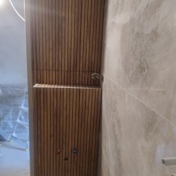 Krys-Bud usługi ogólnobudowlane Krystian Szweda - Drewniana boazeria lamelowa w łazience, z widocznymi otworami na instalacje i częściowo położonymi płytkami. W tle widoczna drabina i folia zabezpieczająca.
