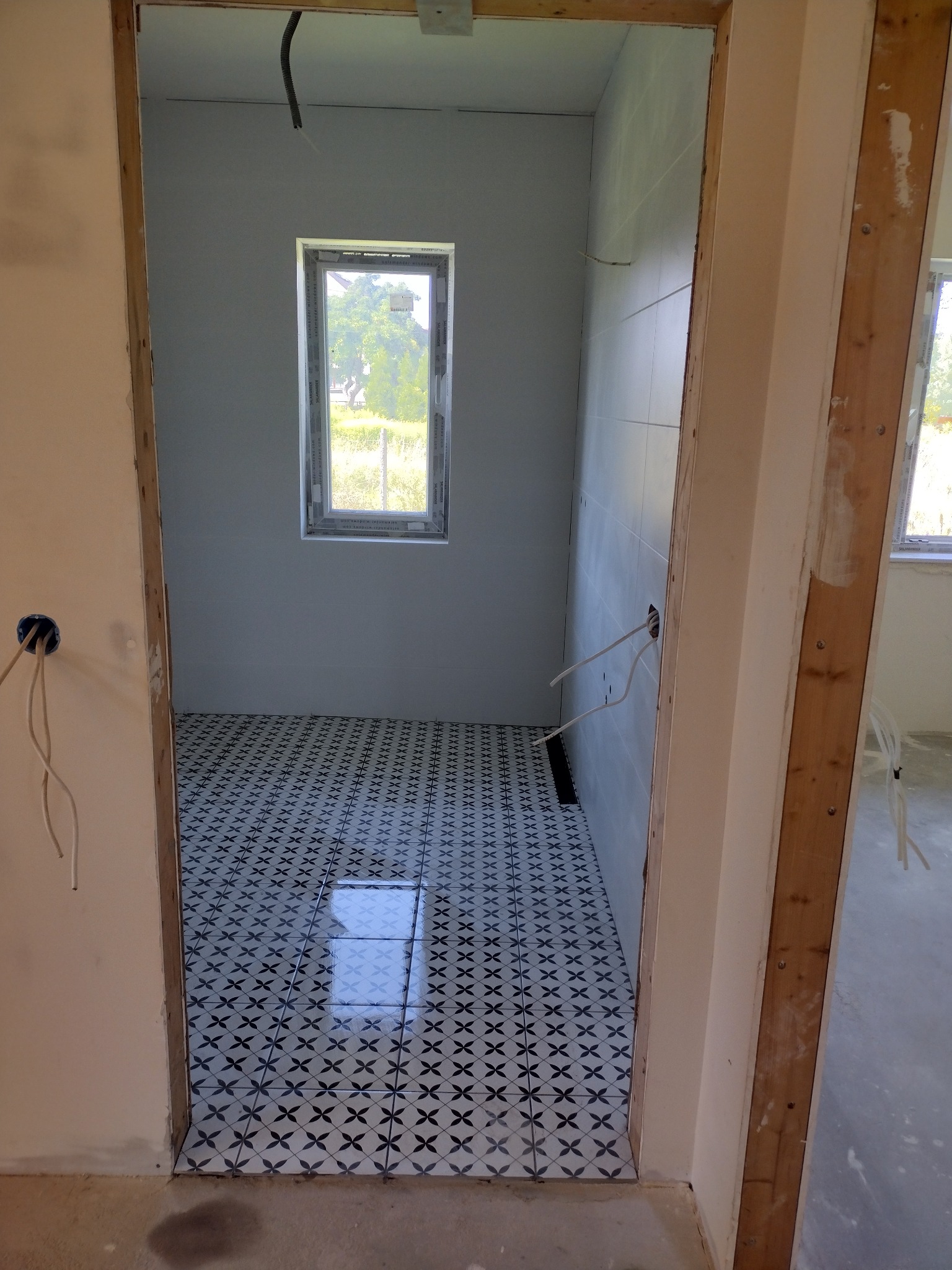 Wykończona podłoga w łazience z wzorzystymi płytkami w Bogunice. Widok zza futryny, świeżo położone płytki z odbiciem światła.