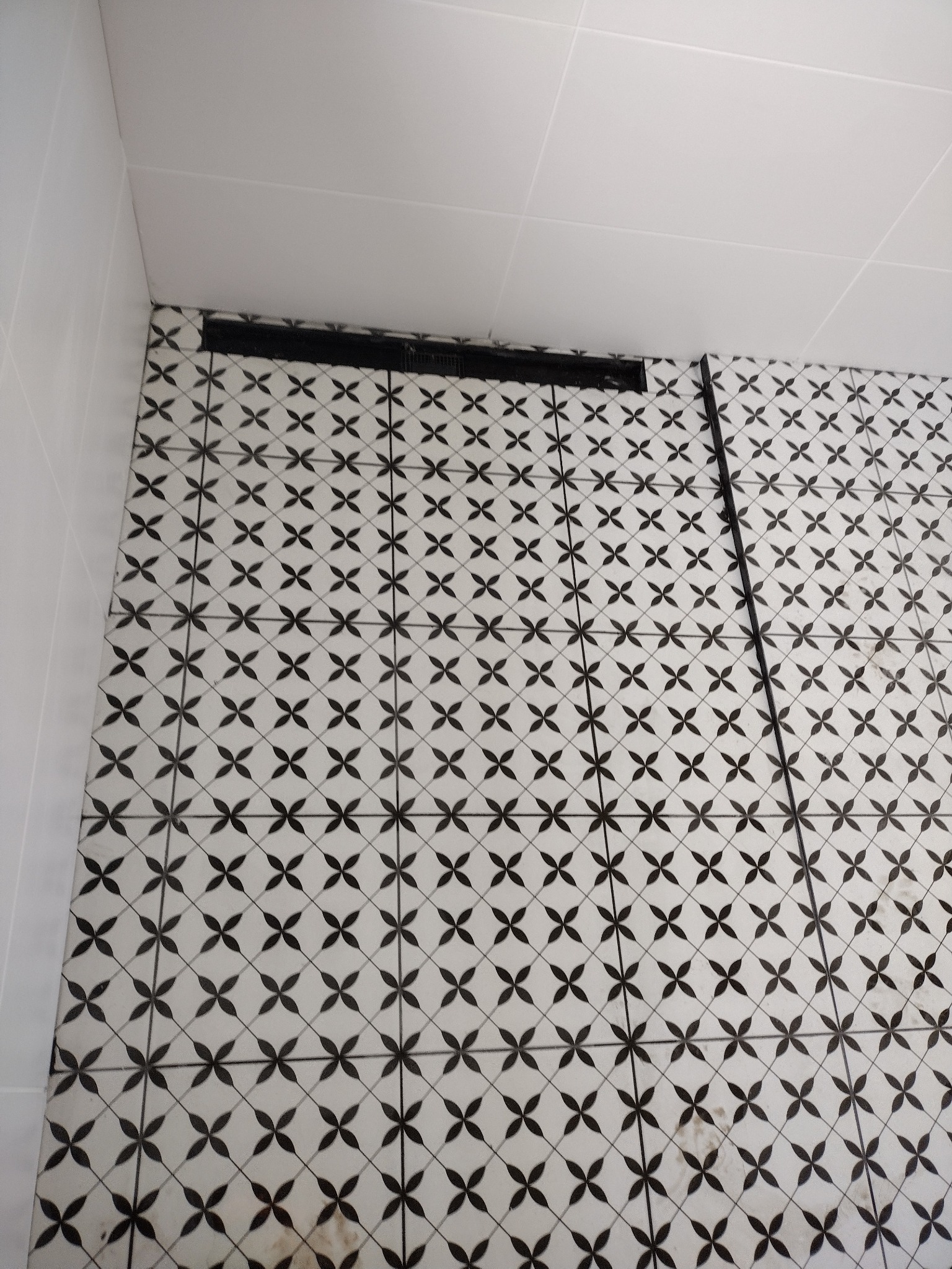 Ukończona podłoga w łazience z czarno-białą wzorzystą glazurą i odpływem liniowym. Widok z góry, płytki ułożone równo.