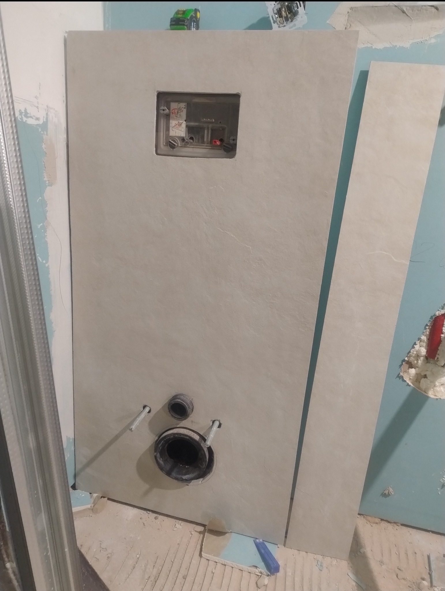 Montaż płyty gipsowej z otworem na stelaż podtynkowy WC. Widoczne rury i instalacja. Fragment metalowego profilu. Prace wykończeniowe w łazience.