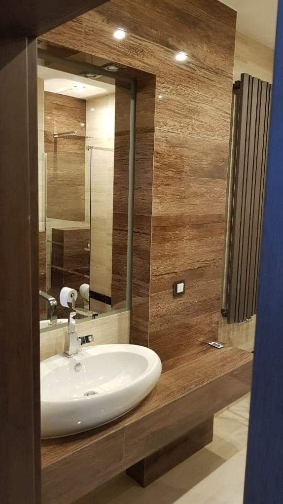 Nowoczesna łazienka z umywalką nablatową, drewnopodobną okładziną ścienną i grzejnikiem drabinkowym.