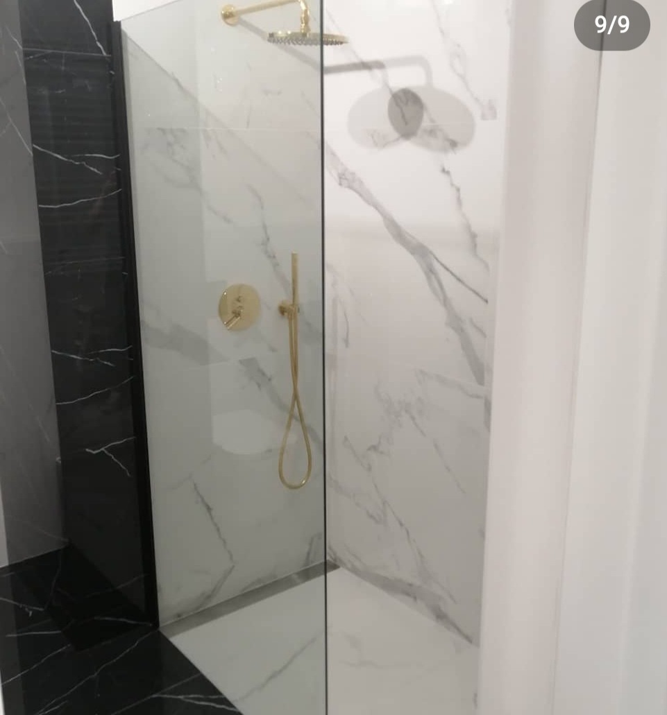 Kabina prysznicowa z białymi i czarnymi marmurowymi płytkami, złota armatura, widok z boku.