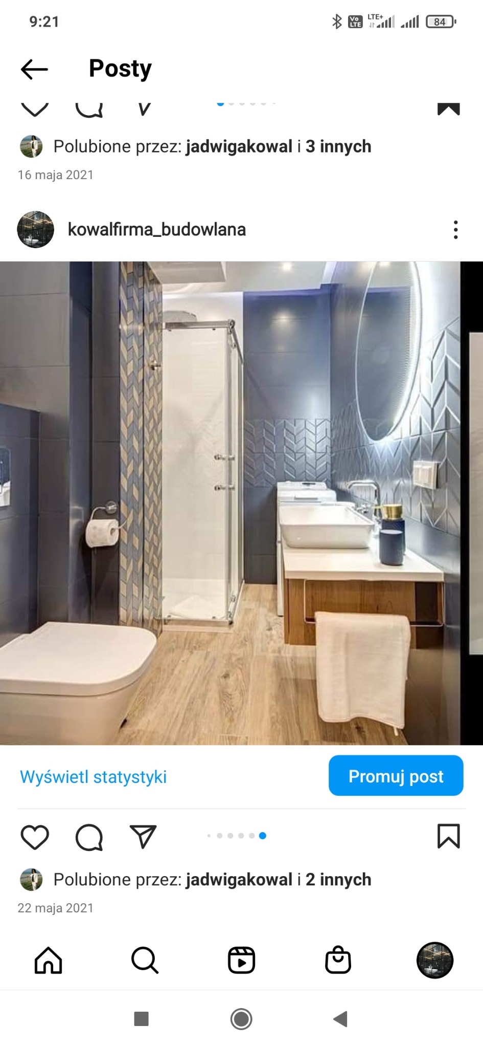 Nowoczesna łazienka w odcieniach szarości i drewna, z kabiną prysznicową, toaletą i umywalką z podświetlanym lustrem, widoczna dekoracyjna ściana z motywem jodełki.