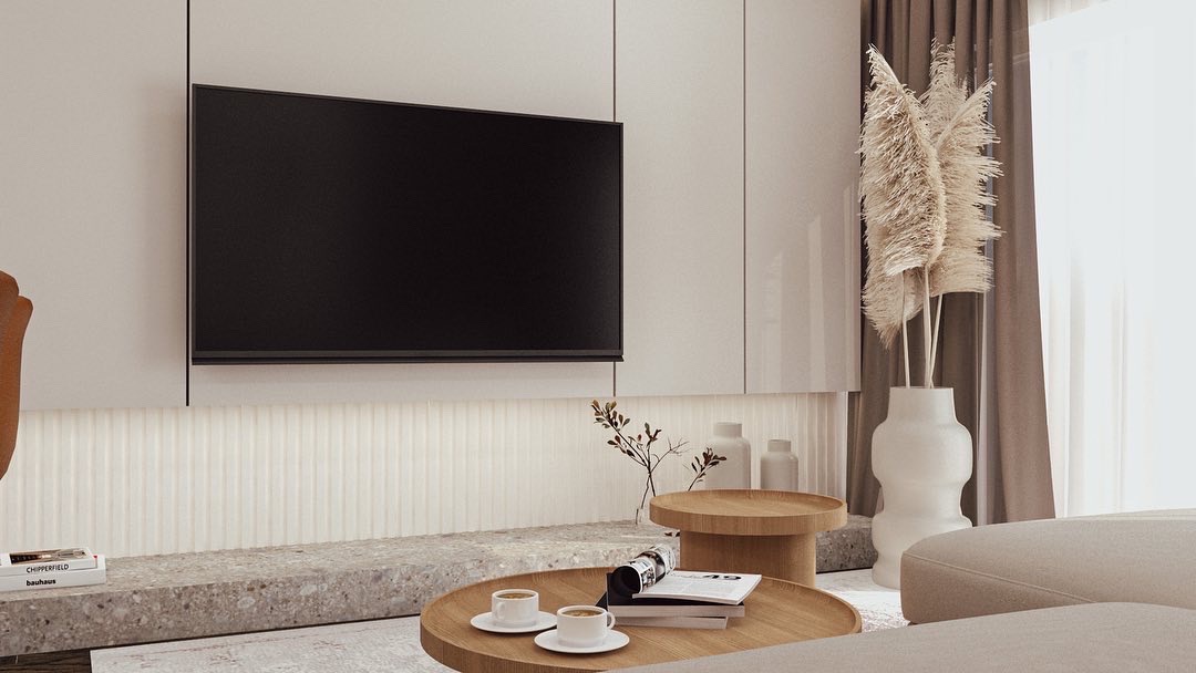 Minimalistyczny salon z telewizorem na ścianie, drewnianymi stolikami kawowymi, dekoracyjną trawą w wazonie i książkami na kamiennym blacie.