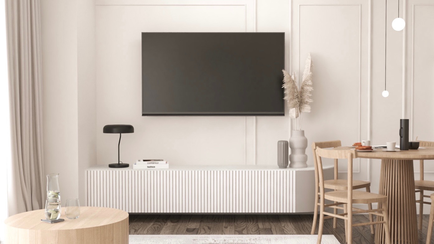 Jasne wnętrze salonu z telewizorem, okrągłym stołem jadalnym z drewnianymi krzesłami, minimalistyczną lampką na szafce RTV oraz szklanym dzbankiem z wodą na okrągłym stoliku kawowym.