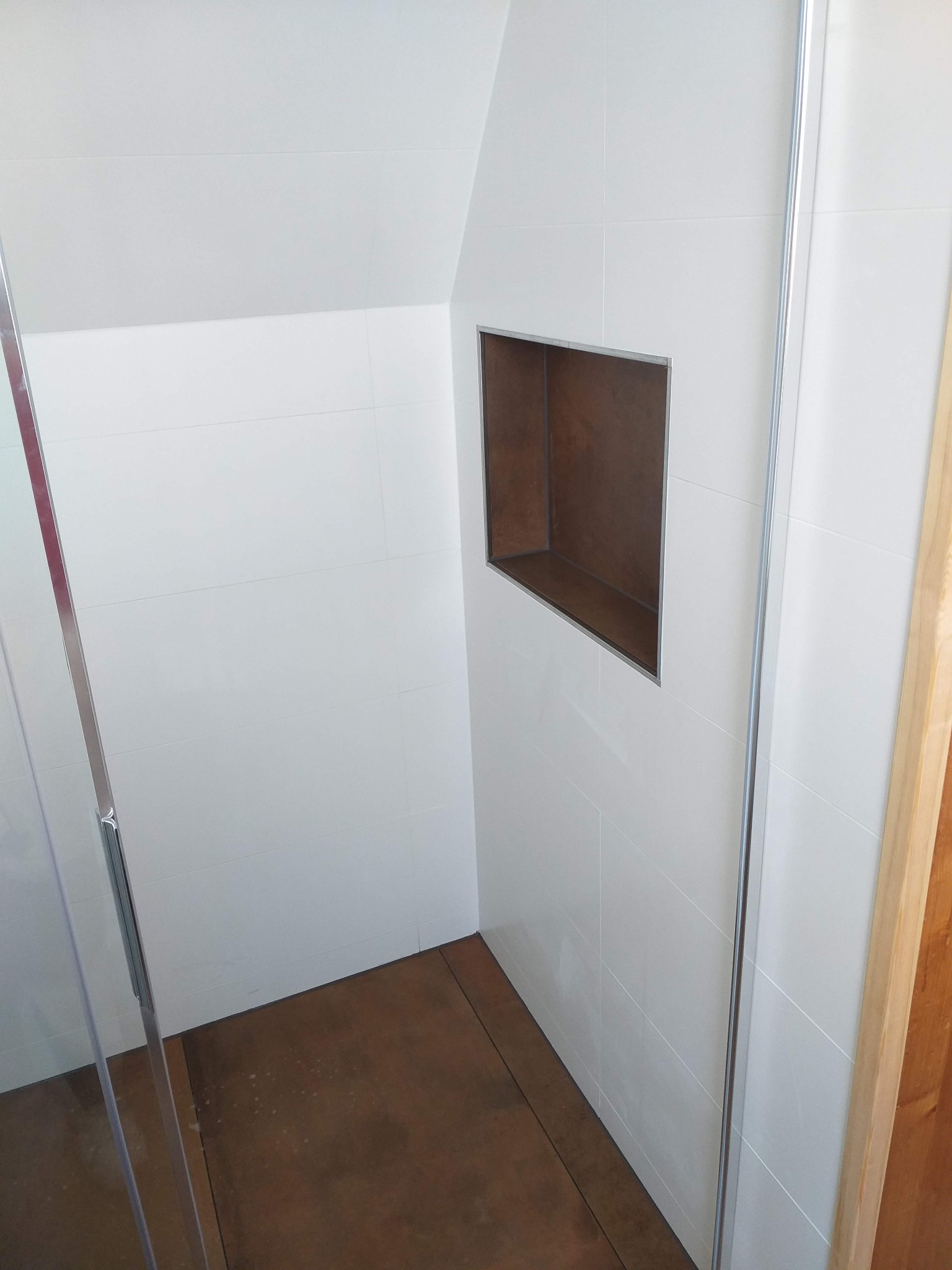 Wykończona łazienka z kabiną prysznicową, białe płytki na ścianach z wnęką wykończoną w brązowym odcieniu, brązowa podłoga.