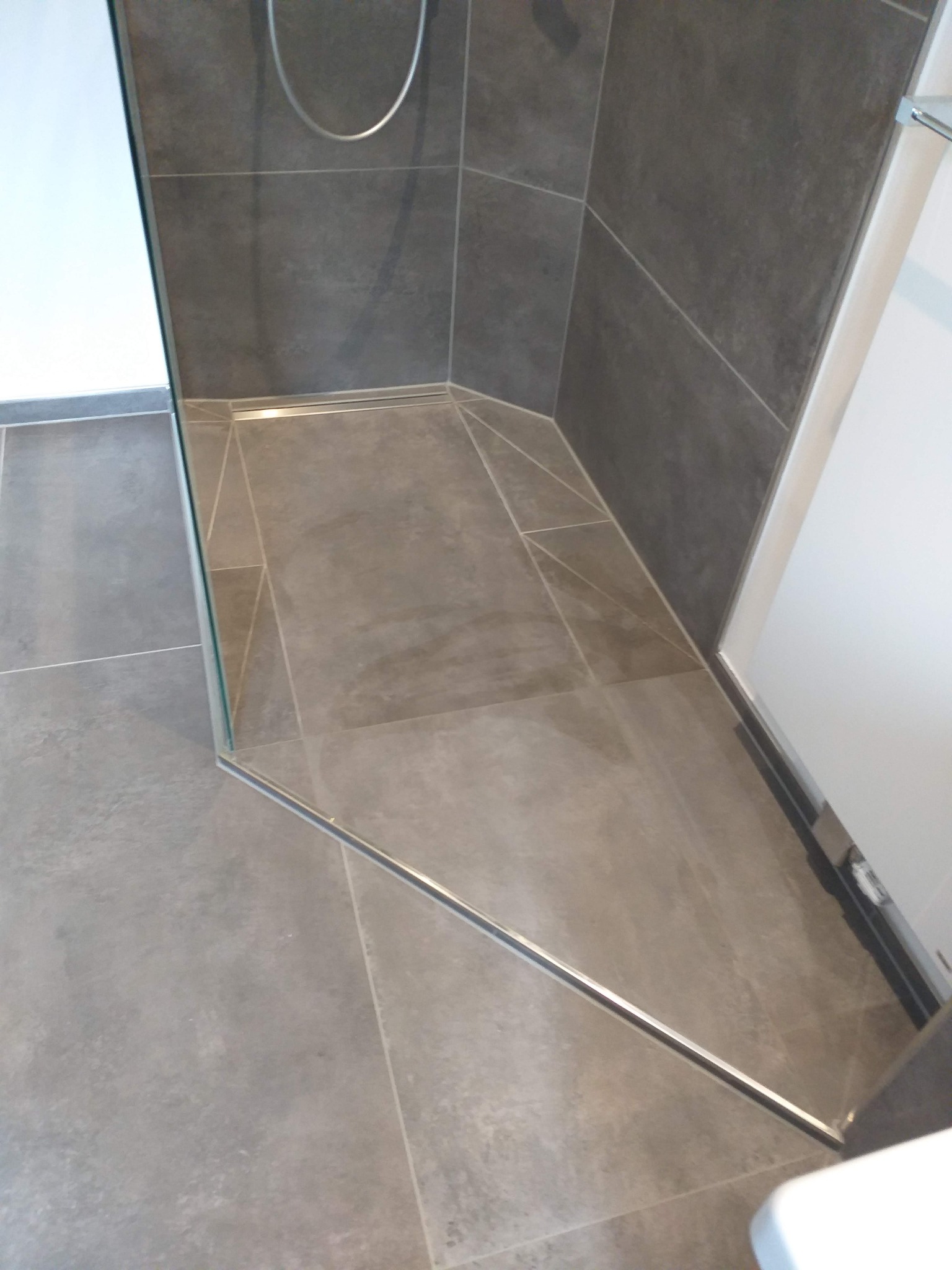 Nowoczesna kabina prysznicowa walk-in z szarymi płytkami i odpływem liniowym w podłodze.