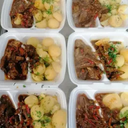 Kilka białych pojemników z gotowym daniem: duszone mięso w sosie z warzywami i gotowane ziemniaki posypane zieloną pietruszką.