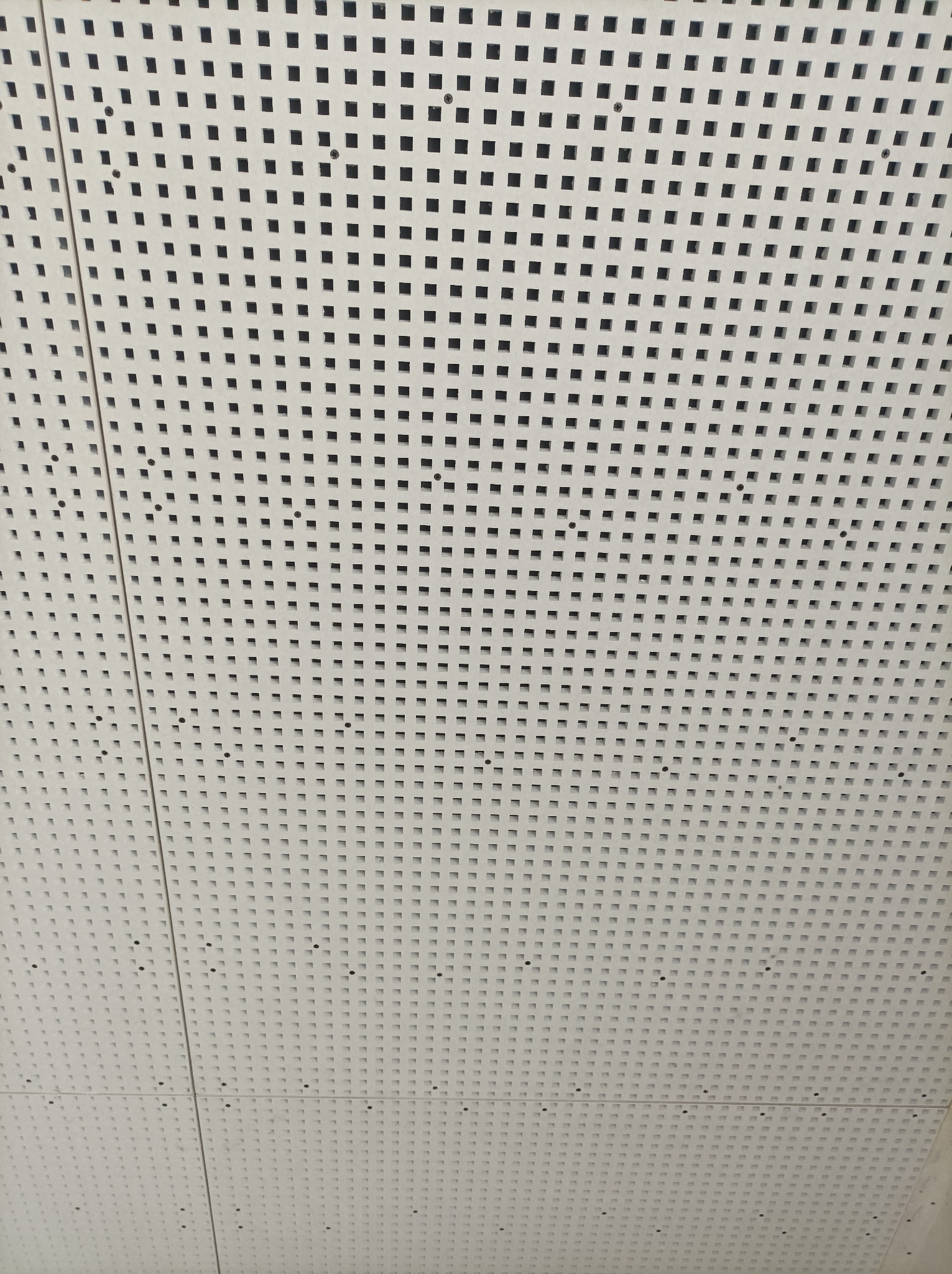 Biały sufit podwieszany z równomiernie rozmieszczonymi kwadratowymi otworami i widocznymi punktami mocowania.