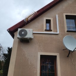 ODNOVA Filip Sidorowicz - Zewnętrzna jednostka klimatyzacji Rotenso zamontowana na elewacji domu jednorodzinnego, widoczna antena telewizyjna i satelitarna.