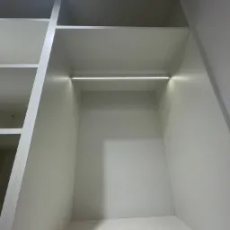 Wnętrze szafy wnękowej z białymi półkami i oświetleniem LED, widok od dołu.