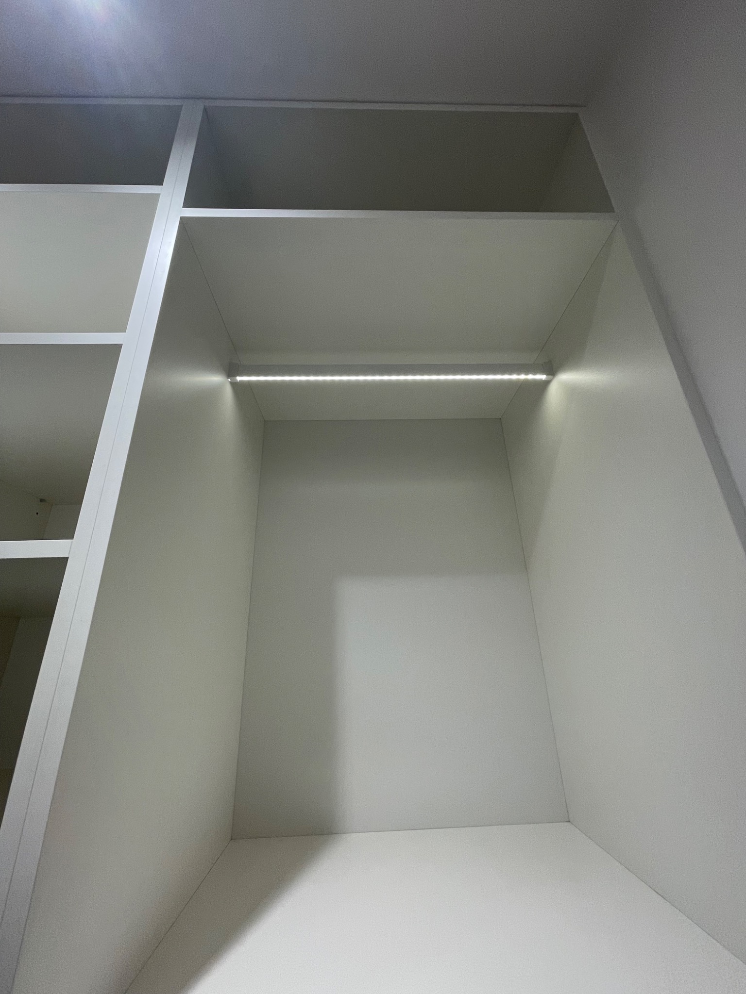 Wnętrze szafy wnękowej z białymi półkami i oświetleniem LED, widok od dołu.