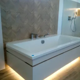 Nowoczesna wanna z podświetleniem LED, umieszczona na tle ściany wyłożonej płytkami w jodełkę, z widoczną armaturą i kabiną prysznicową w tle.