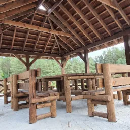 Drewniana altana z kompletem mebli ogrodowych wykonanych z okrąglaków, widok na las w tle.