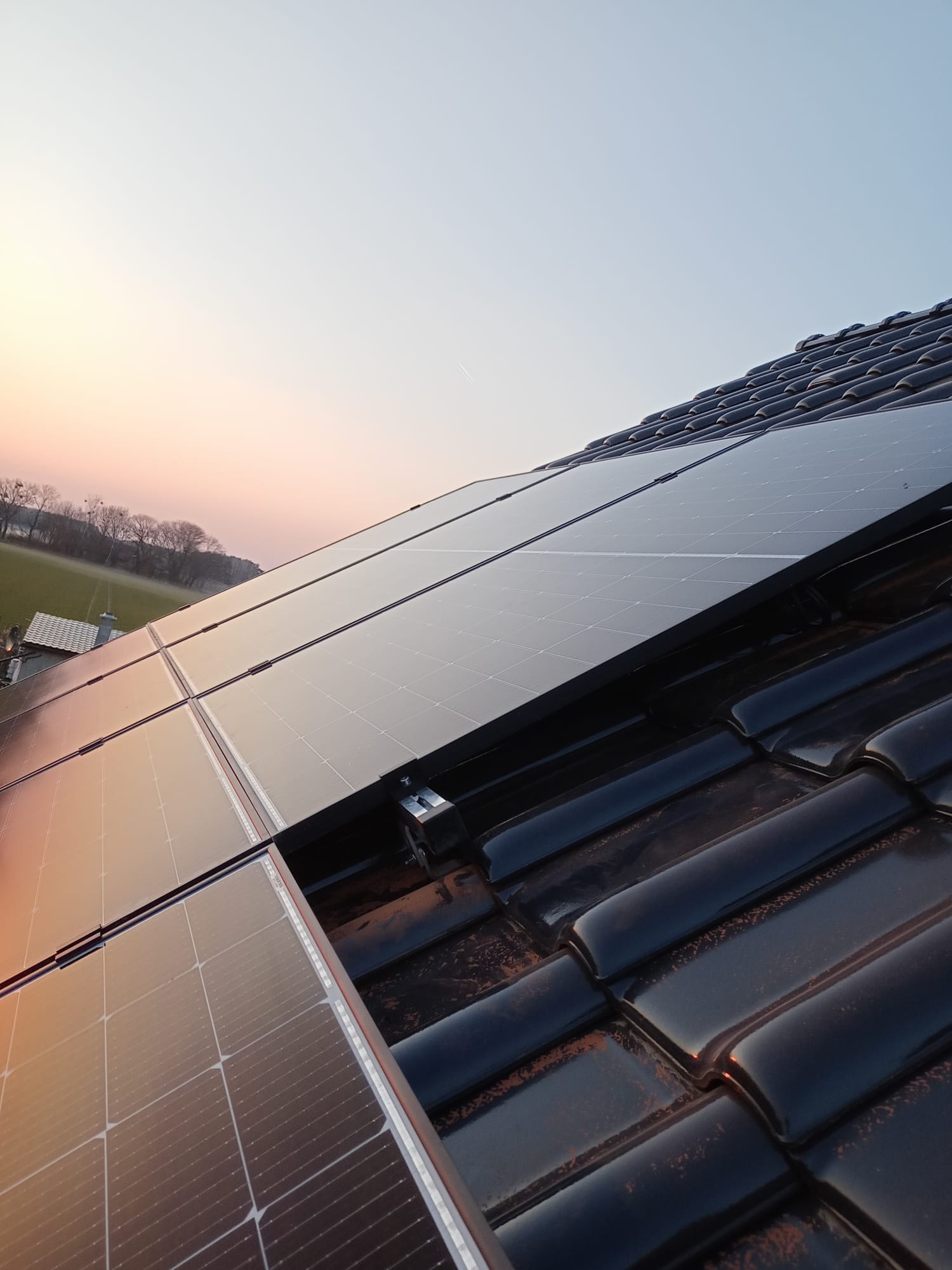 Panele słoneczne na dachu z czarnej dachówki, widok pod kątem, zachód słońca w tle.