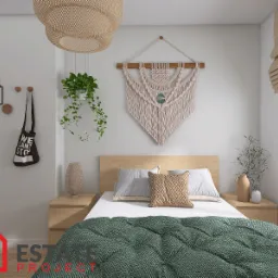 Jasna sypialnia z drewnianym zagłówkiem, zieloną kołdrą w romby, makramą na ścianie, wiszącą rośliną i rattanową lampą, widok z przodu.