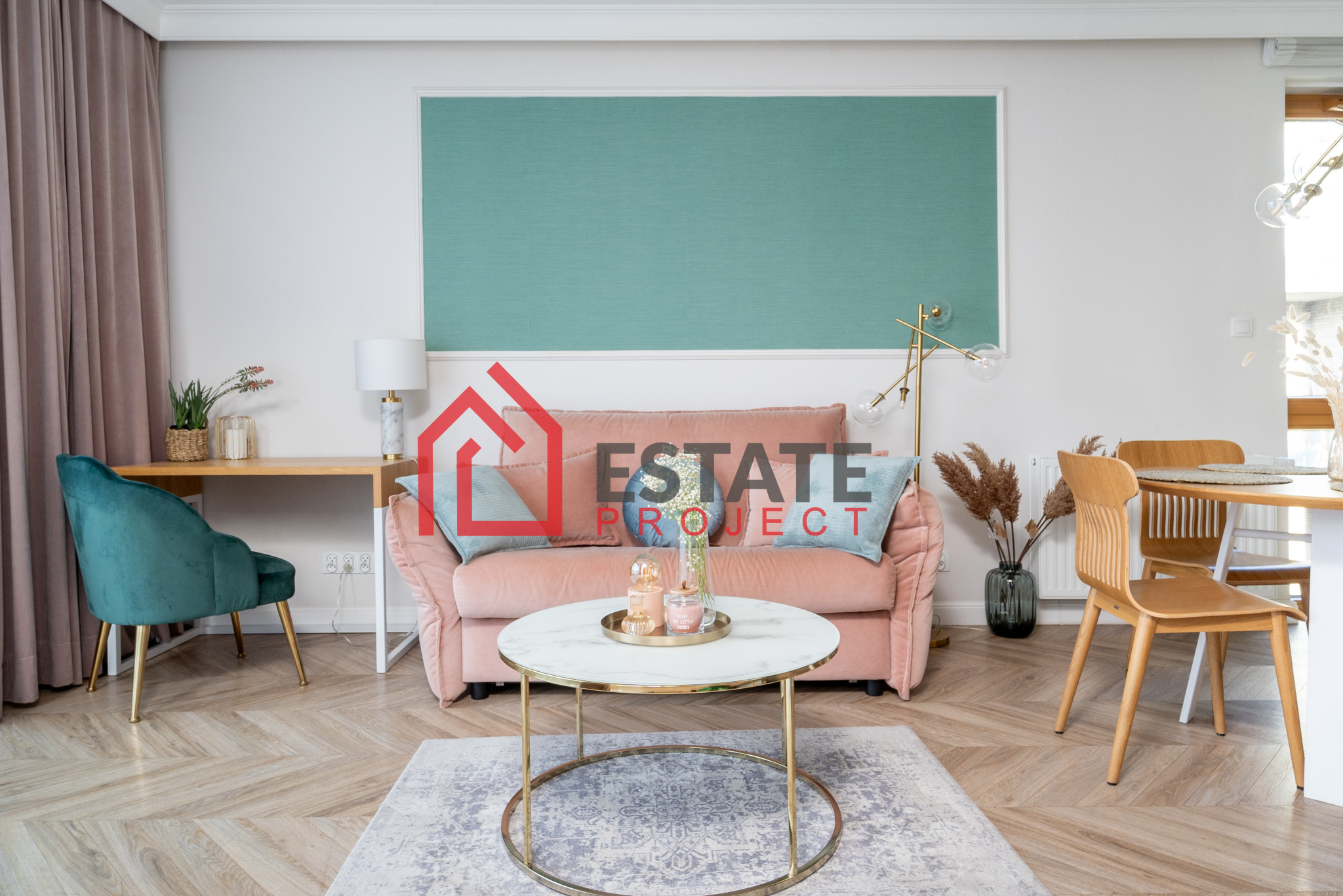 Jasne wnętrze salonu z parkietem w jodełkę, różową sofą, okrągłym stolikiem kawowym z marmurowym blatem, turkusowym akcentem kolorystycznym i zasłonami w kolorze pudrowego różu.