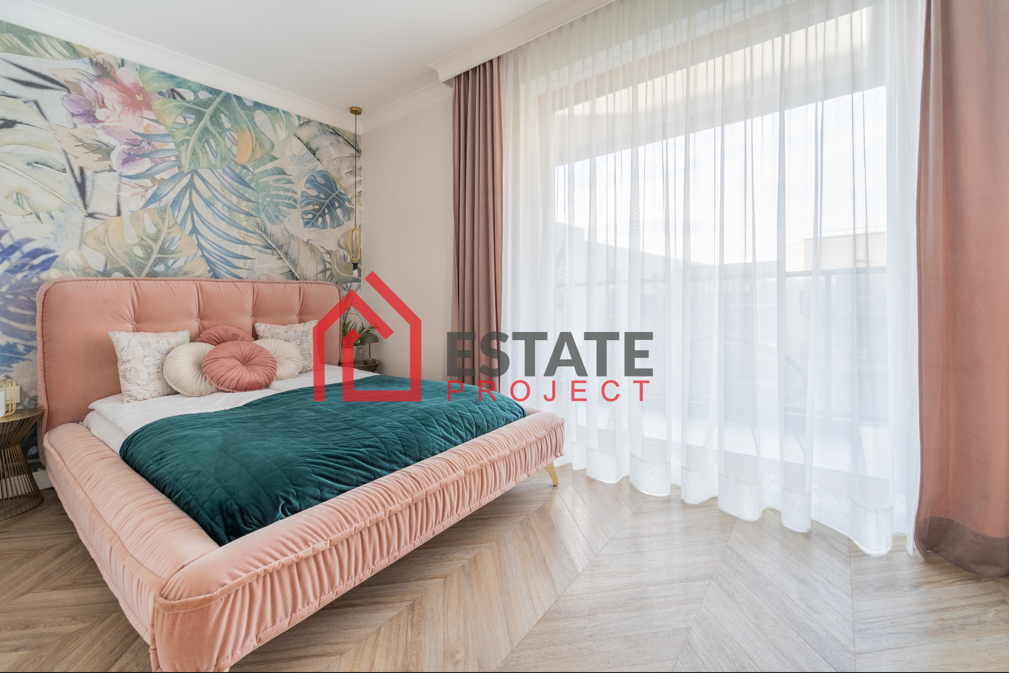 Sypialnia z łóżkiem w pudrowym różu, zieloną narzutą i tapetą w tropikalne liście, widok na okno z firankami i zasłonami.