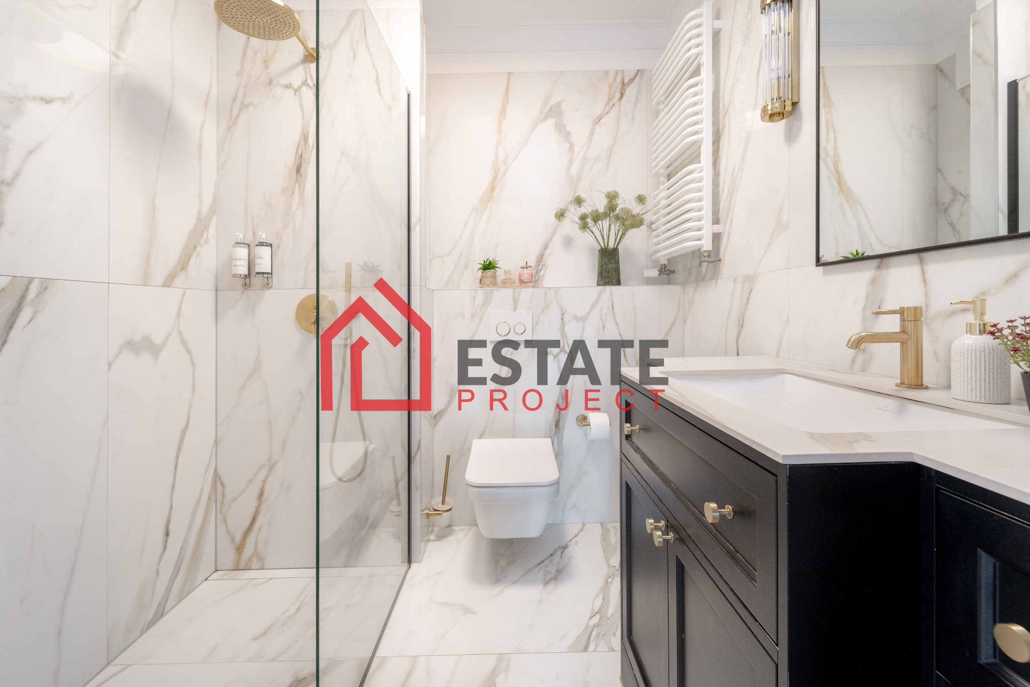 Elegancka łazienka z kabiną prysznicową typu walk-in, marmurowymi płytkami, toaletą podwieszaną i czarną szafką pod umywalką z złotymi akcentami.