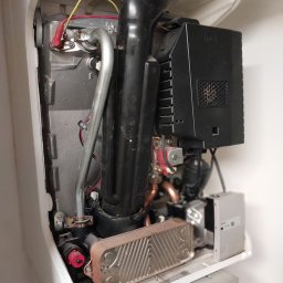 HEAT MASTER SERWIS URZĄDZEŃ GAZOWYCH Marcin Rudzik - Wnętrze otwartego kotła gazowego z widocznymi komponentami: wymiennikiem ciepła, rurami, przewodami elektrycznymi oraz elementami sterującymi, w trakcie przeglądu technicznego.