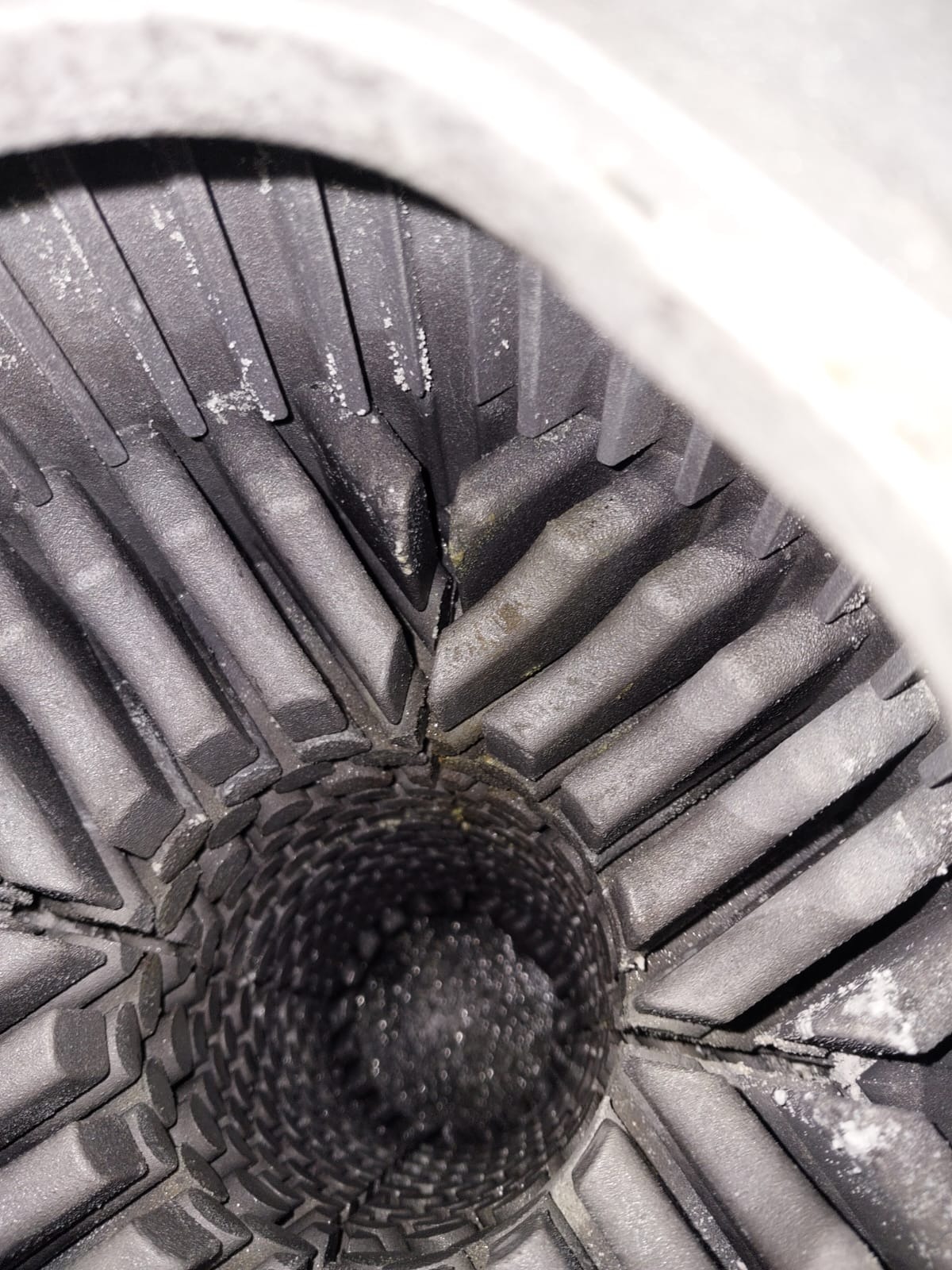 Wnętrze komory spalania pieca gazowego, widoczne żebra chłodzące i otwór wylotowy, pokryte osadem i śladami korozji.