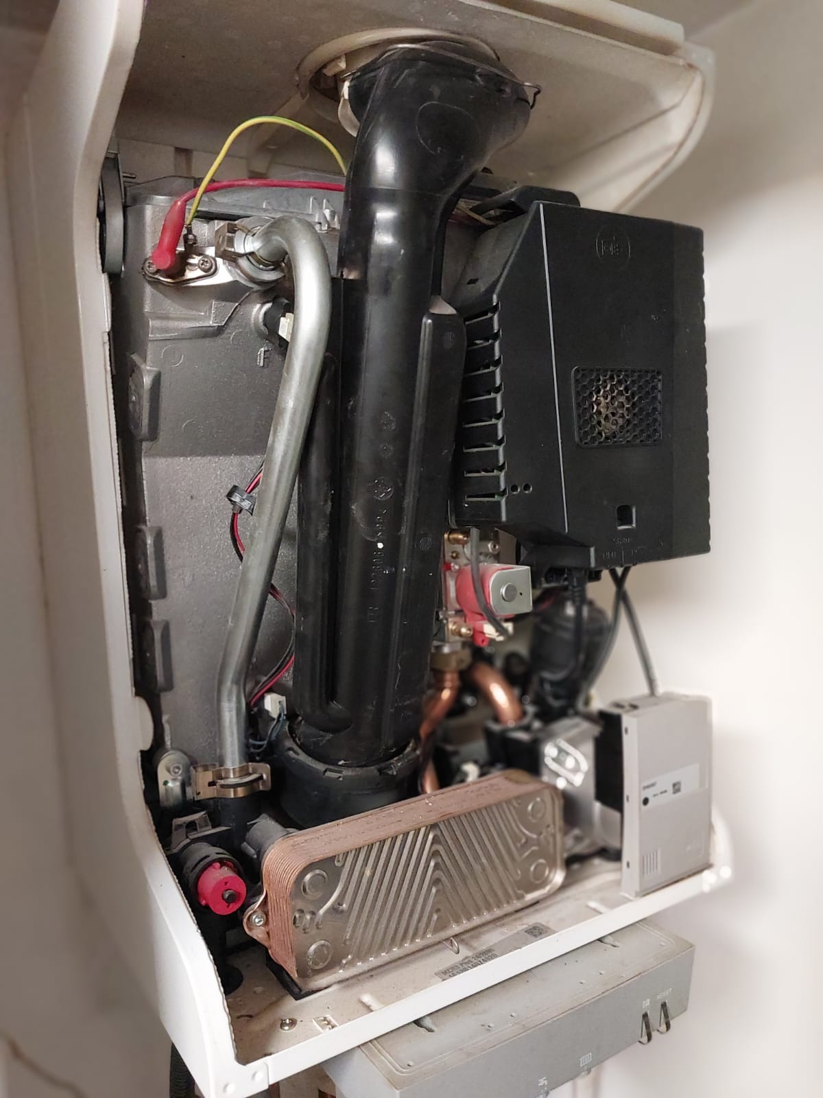 Wnętrze otwartego kotła gazowego z widocznymi komponentami: wymiennikiem ciepła, rurami, przewodami elektrycznymi oraz elementami sterującymi, w trakcie przeglądu technicznego.