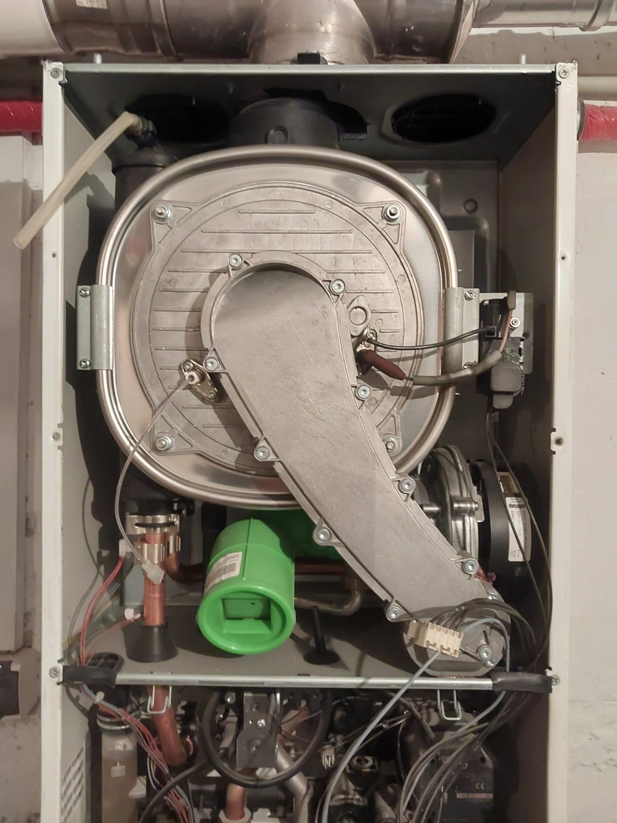 Wnętrze obudowy pieca gazowego z widocznym wentylatorem, elementami instalacji i zielonym komponentem, sfotografowane z bliska.