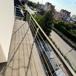 Dagmat - Błyszcząca, stalowa balustrada balkonowa z widokiem na osiedle w słoneczny dzień. Minimalistyczny design, proste linie, nowoczesne wykończenie balkonu.
