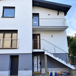 Dagmat - Nowoczesny dom z zewnętrznymi schodami i balustradami ze stali nierdzewnej na balkonach, widok z dołu, jasna elewacja.