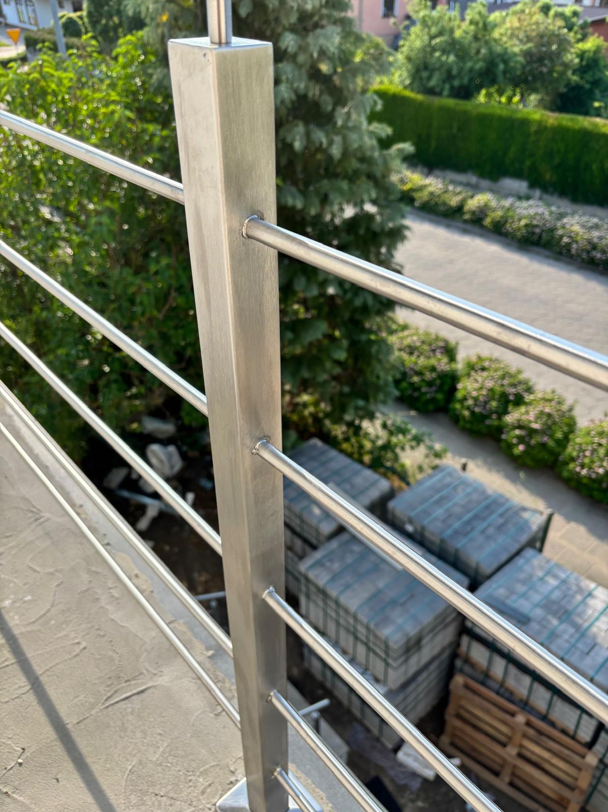 Nowoczesna balustrada ze stali nierdzewnej z poziomymi prętami, widok z góry, w tle zieleń i kostka brukowa, świeże spawanie, minimalizm.