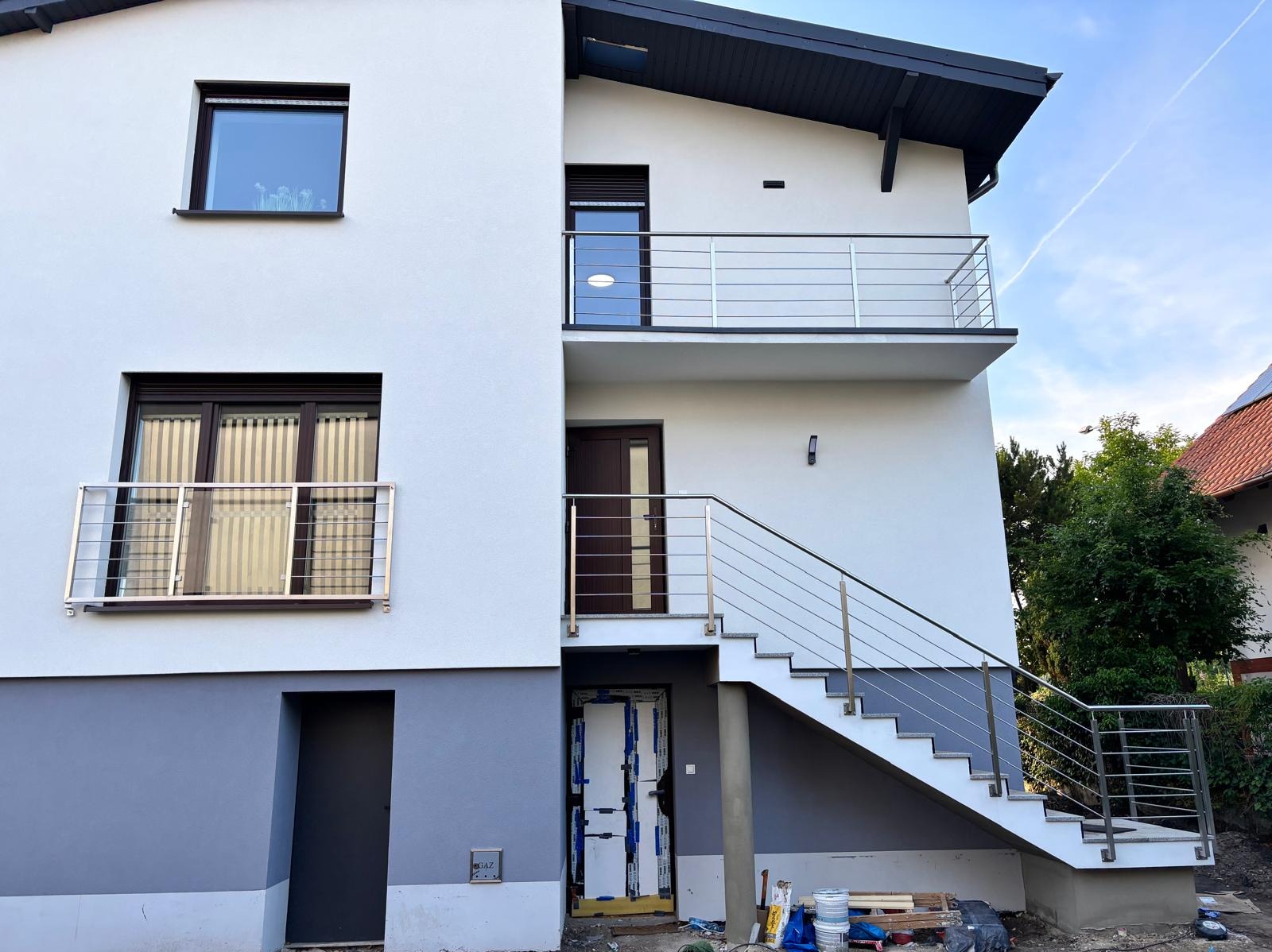 Nowoczesny dom z zewnętrznymi schodami i balustradami ze stali nierdzewnej na balkonach, widok z dołu, jasna elewacja.