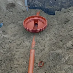 Wykonany wykop z widoczną studzienką kanalizacyjną z tworzywa sztucznego, fragmentem rury kanalizacyjnej i pierścieniem uszczelniającym w ziemi.