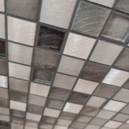 Mozaika ścienna z kwadratowych płytek w odcieniach beżu i brązu, ułożona pod kątem, z widocznymi fugami.