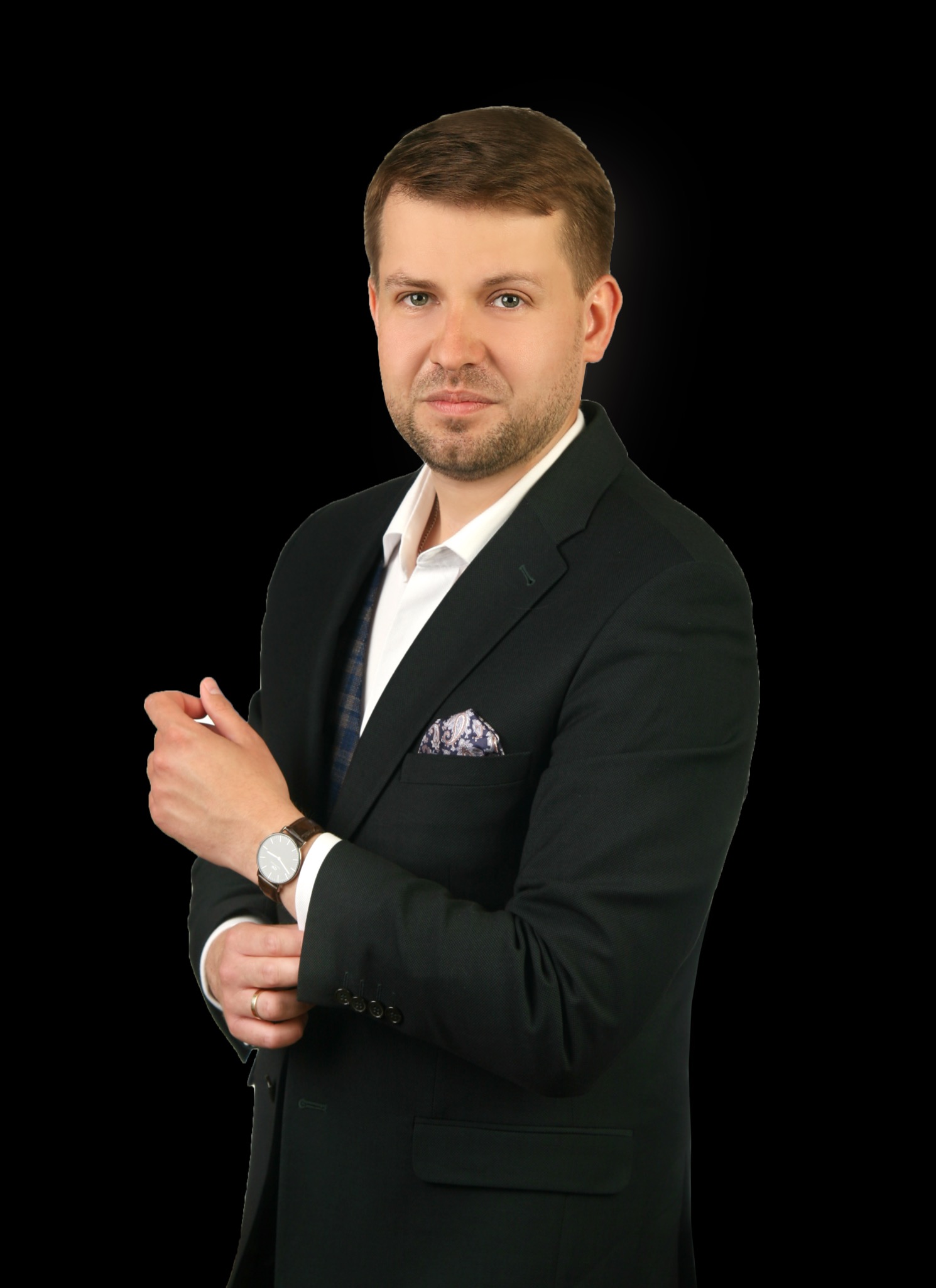 Portret mężczyzny w ciemnozielonym garniturze, białej koszuli i kamizelce, poprawiającego mankiet koszuli, z zegarkiem na nadgarstku i złotą obrączką na palcu, na czarnym tle.