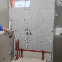 Montaż płytek z geometrycznym wzorem w łazience, widoczne krzyżyki dystansowe, poziomica laserowa, profile i narzędzia glazurnicze.