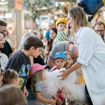 Kobieta w białej koszuli demonstruje efektowne wytwarzanie dymu dla grupy dzieci w jasnym, przestronnym pomieszczeniu, prawdopodobnie w centrum handlowym. Dzieci z zaciekawieniem obserwują...