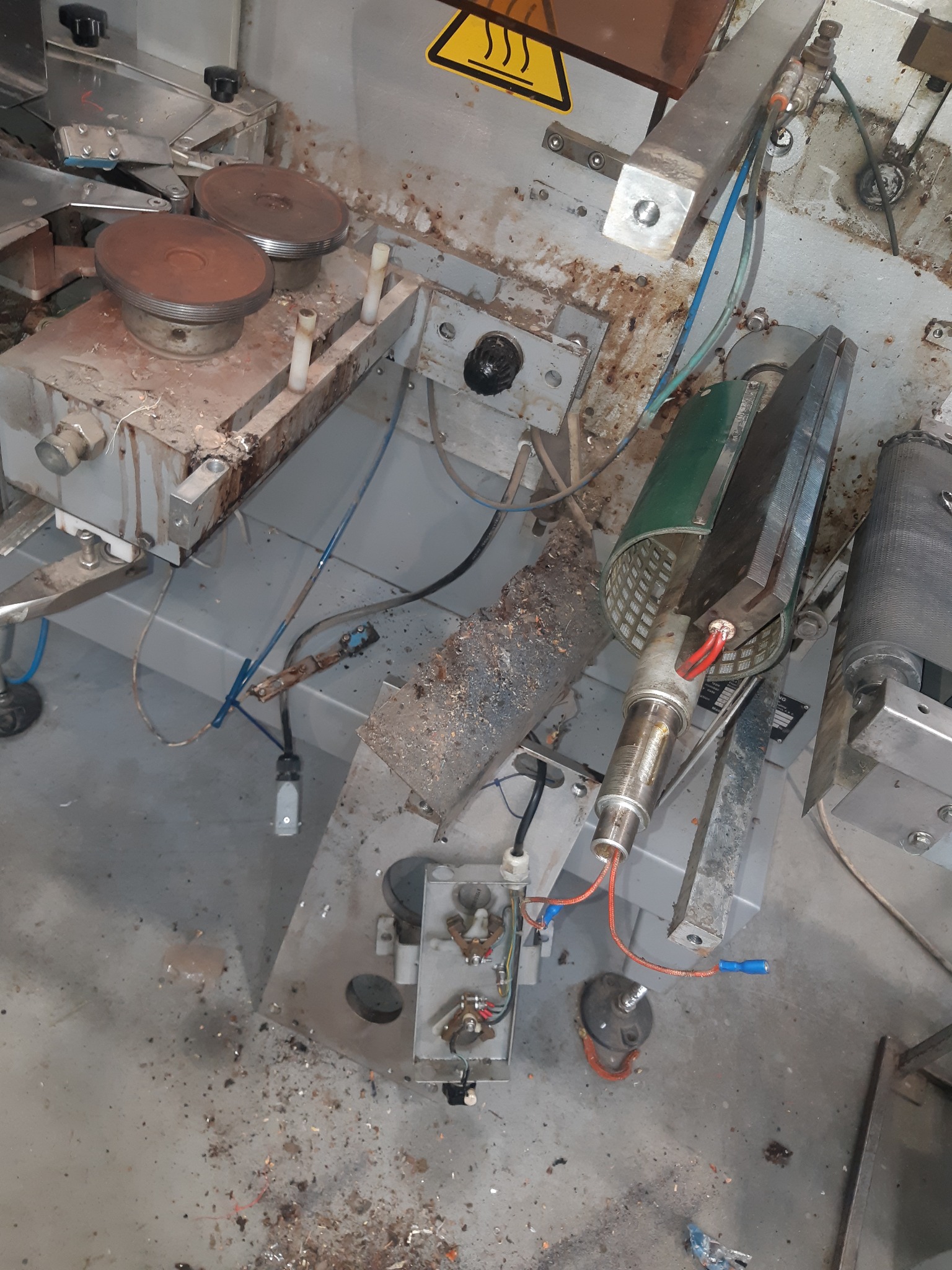 Widok z góry na brudną, przemysłową maszynę z elementami grzejnymi i przewodami, wymagającą czyszczenia i konserwacji.