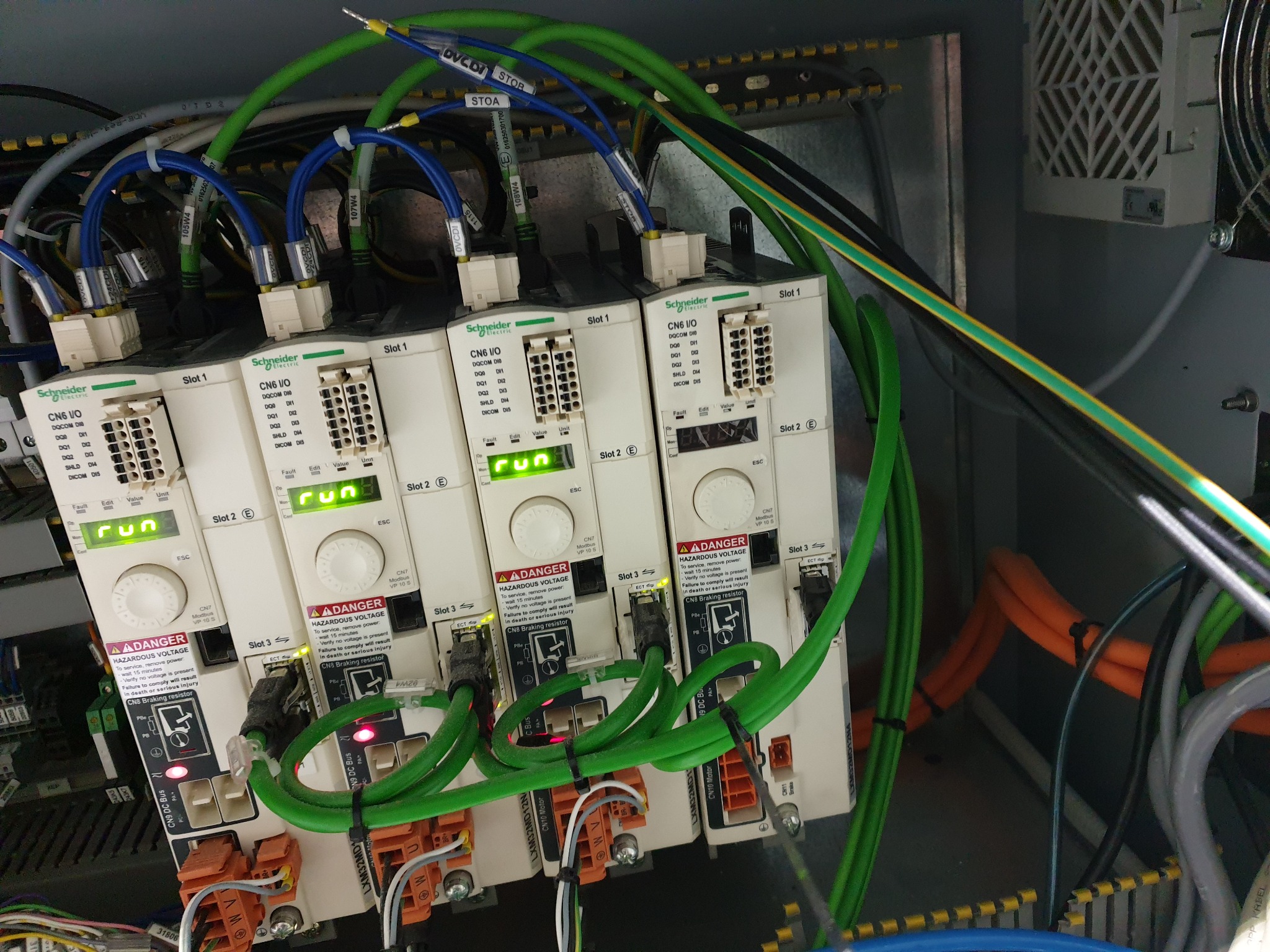 Panel sterowania maszyny z modułami Schneider Electric CN6 I/O, okablowaniem i oznaczeniami, widoczne diody sygnalizacyjne i ostrzeżenia o wysokim napięciu.
