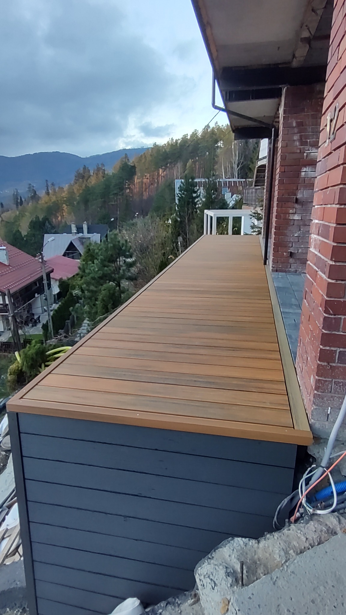 Nowoczesny taras kompozytowy z widokiem na góry w Jasienicy, z szarą obudową i drewnopodobną powierzchnią, częściowo widoczne instalacje elektryczne.